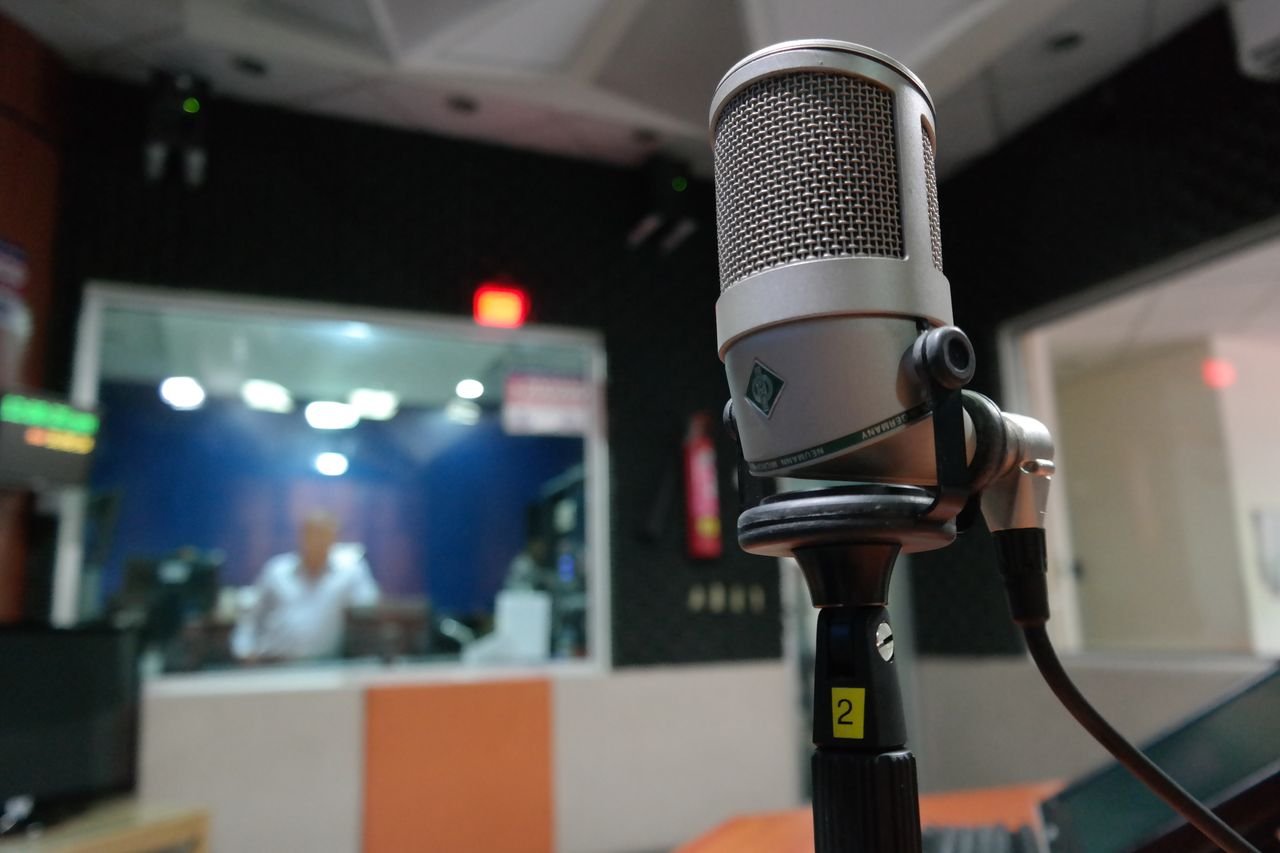 Home Close-up of a microphone in a recording studio with a blurred sound engineer in the background.